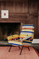 Chair upholstered in Anni Albers Hanging 1925 fabric, a woven collaboration with the Josef and Anni Albers Foundation, set against paneled wooden walls and complemented by mid-century modern 1960s style furniture. Now Archived.